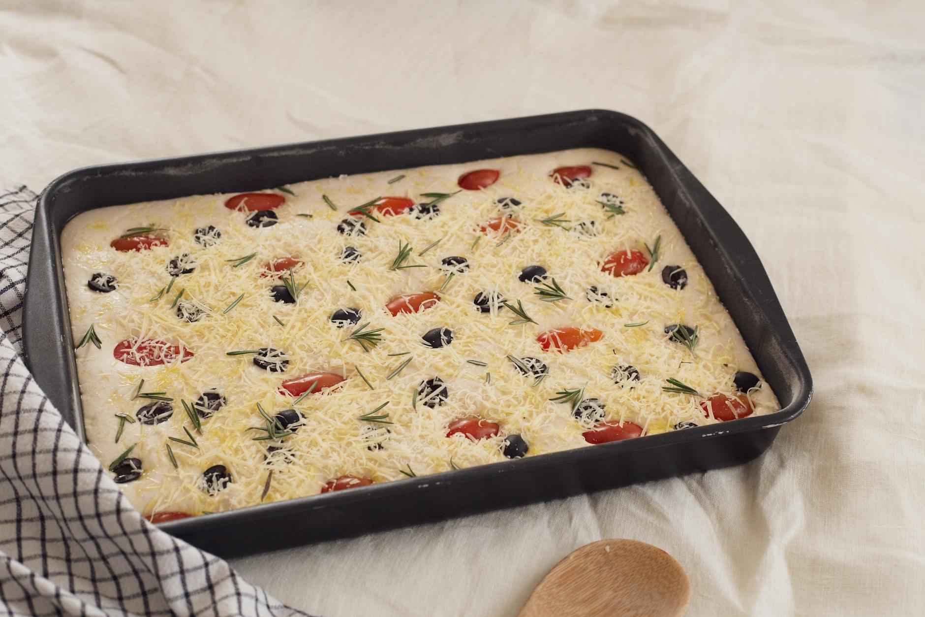 Surowe ciasto drożdżowe focaccia z serem, oliwkami, pomidorami i rozmarynem