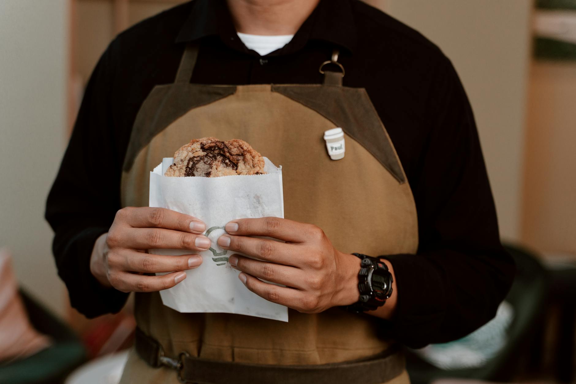 Barista w fartuchu trzyma świeżo upieczone ciasteczko w kawiarni