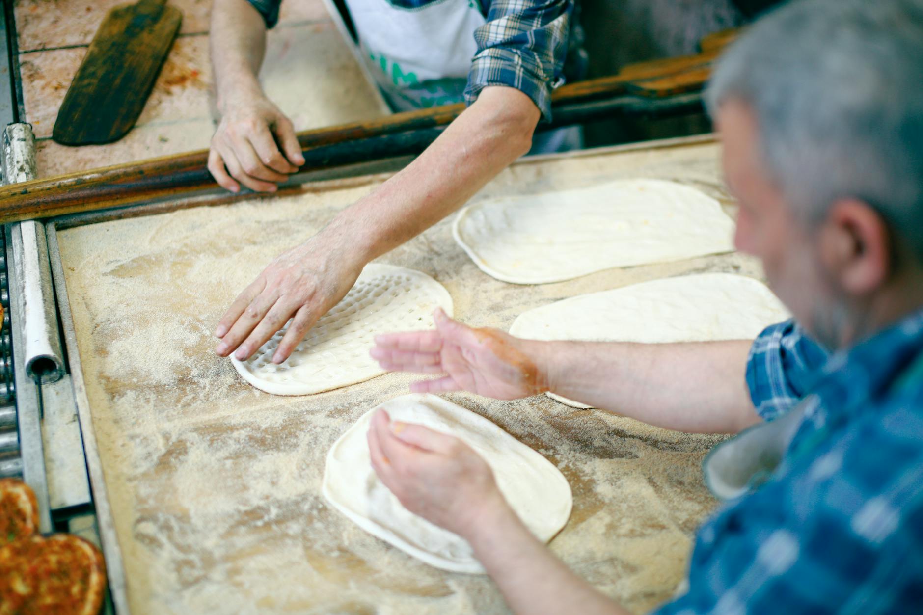 Dwóch piekarzy formuje płaskie chleby z ciasta na obsypanym mąką blacie
