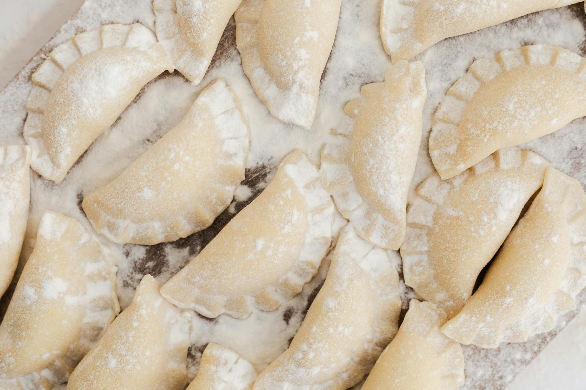 Surowe pierogi na drewnianej tacy oprószone mąką, przygotowane do gotowania