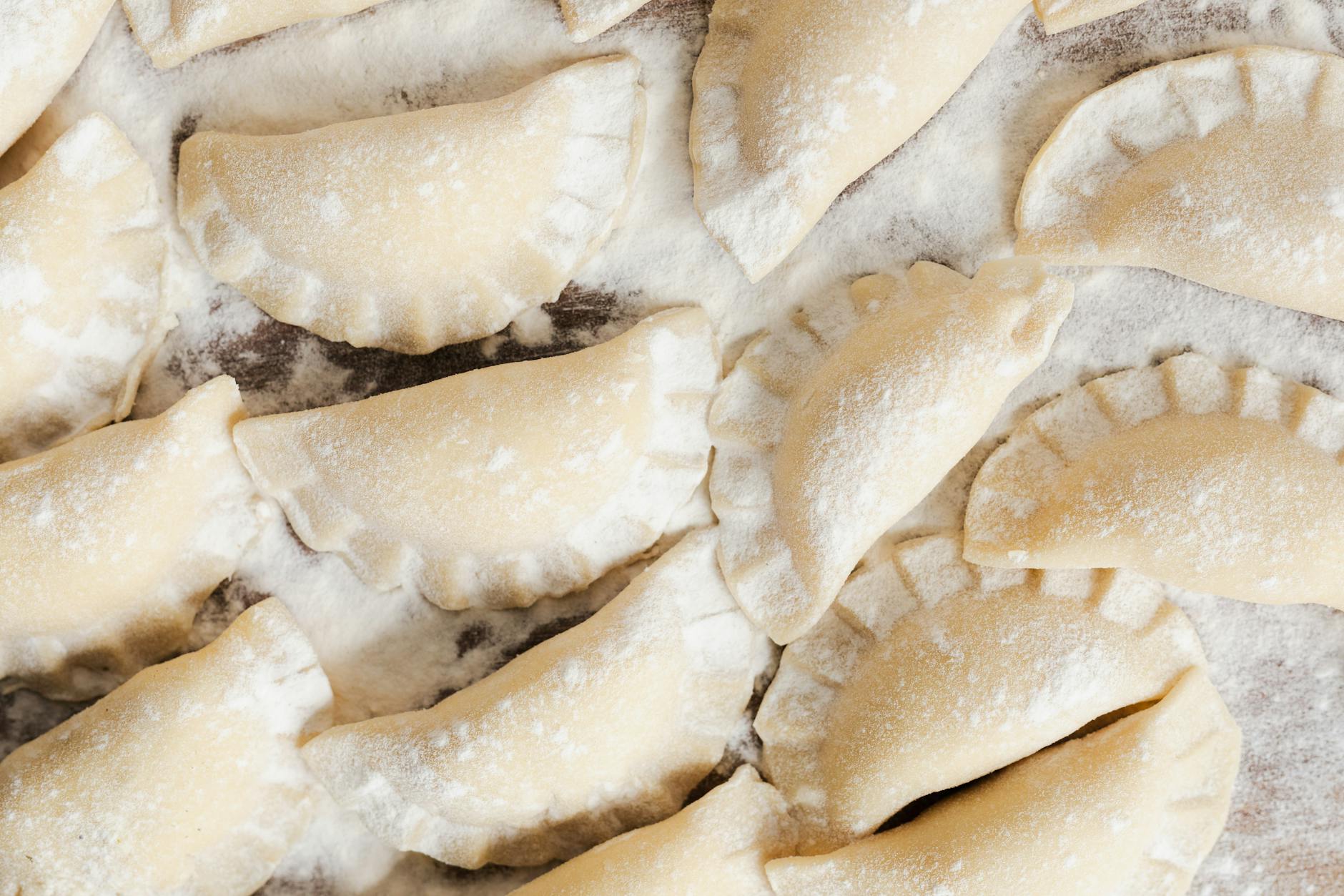 Surowe pierogi ułożone na oprószonym mąką blacie z góry