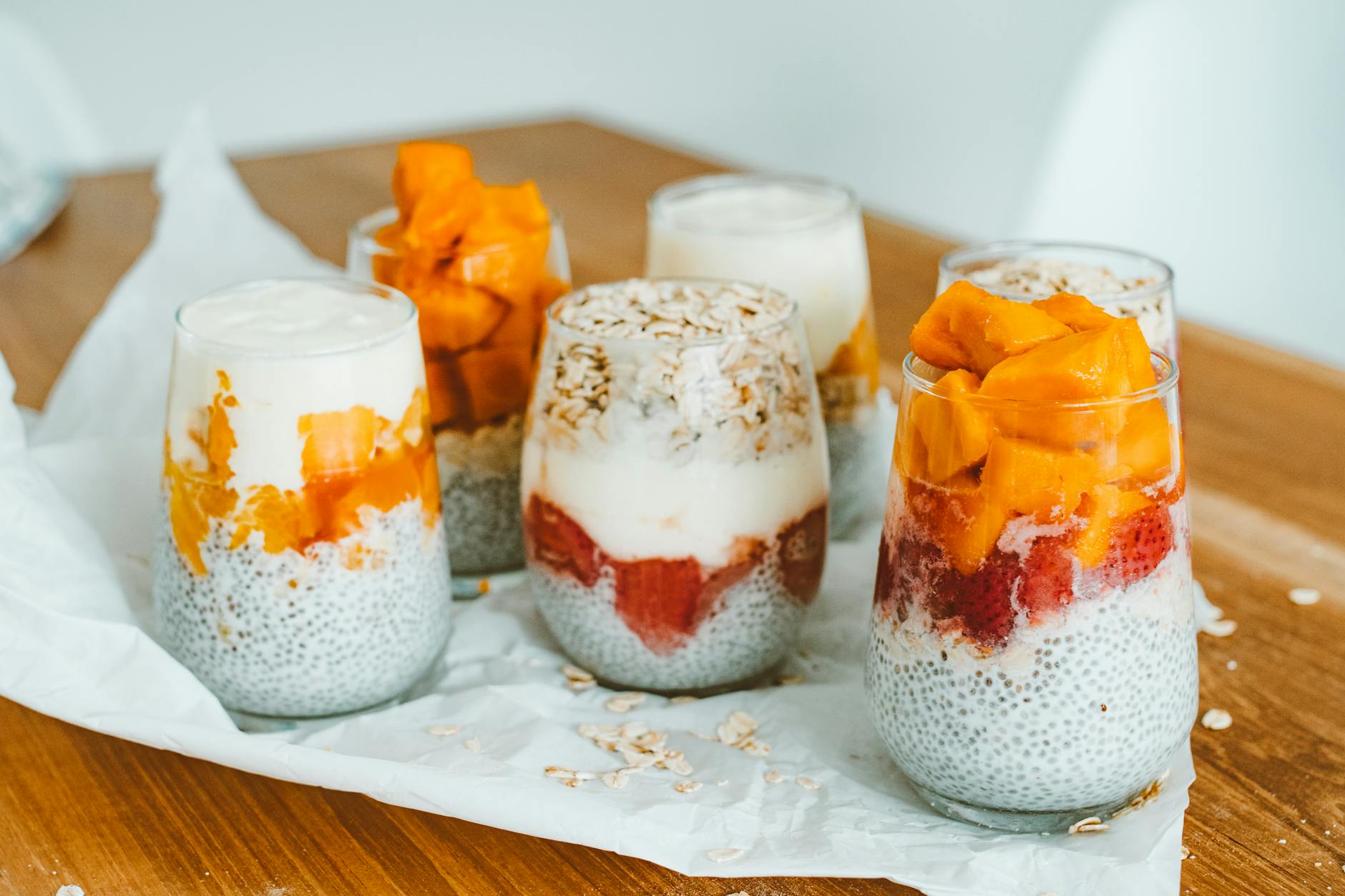 Pucharki chia z warstwami mango i truskawek na drewnianym stole