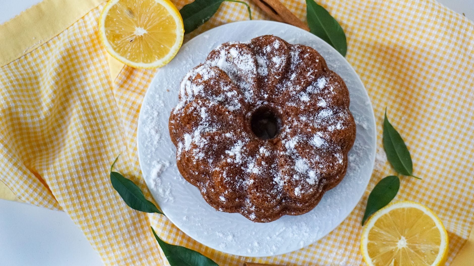 Babka cytrynowa z cukrem pudrem na paterze, obok plasterki cytryny