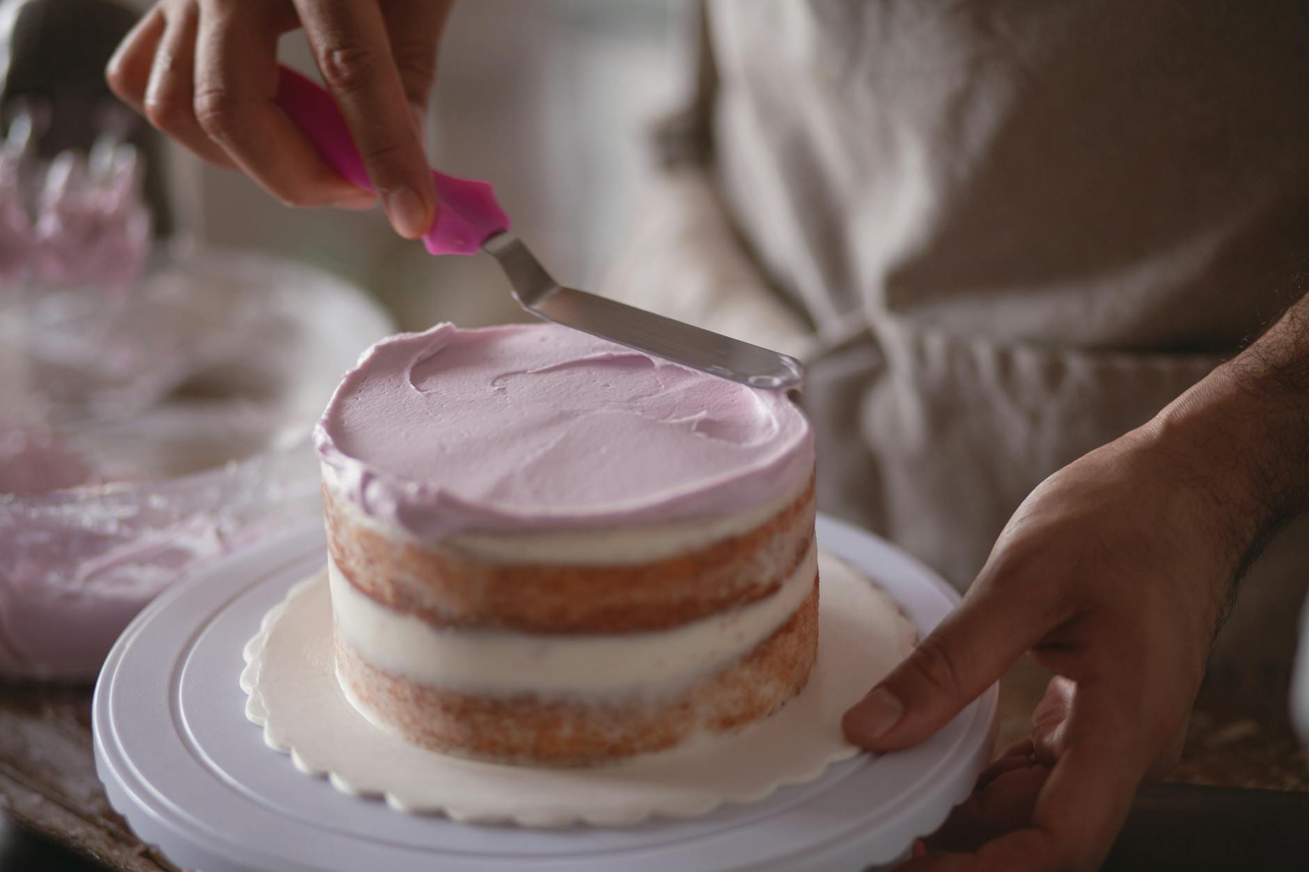 Cukiernik wygładza tynk na jasnym torcie pastelowym kremem