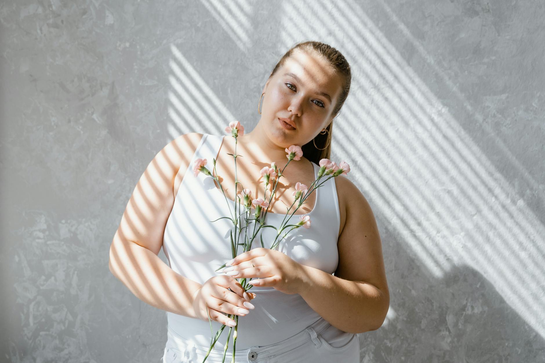 Uśmiechnięta kobieta plus size z kwiatami w świetle przechodzącym przez żaluzje