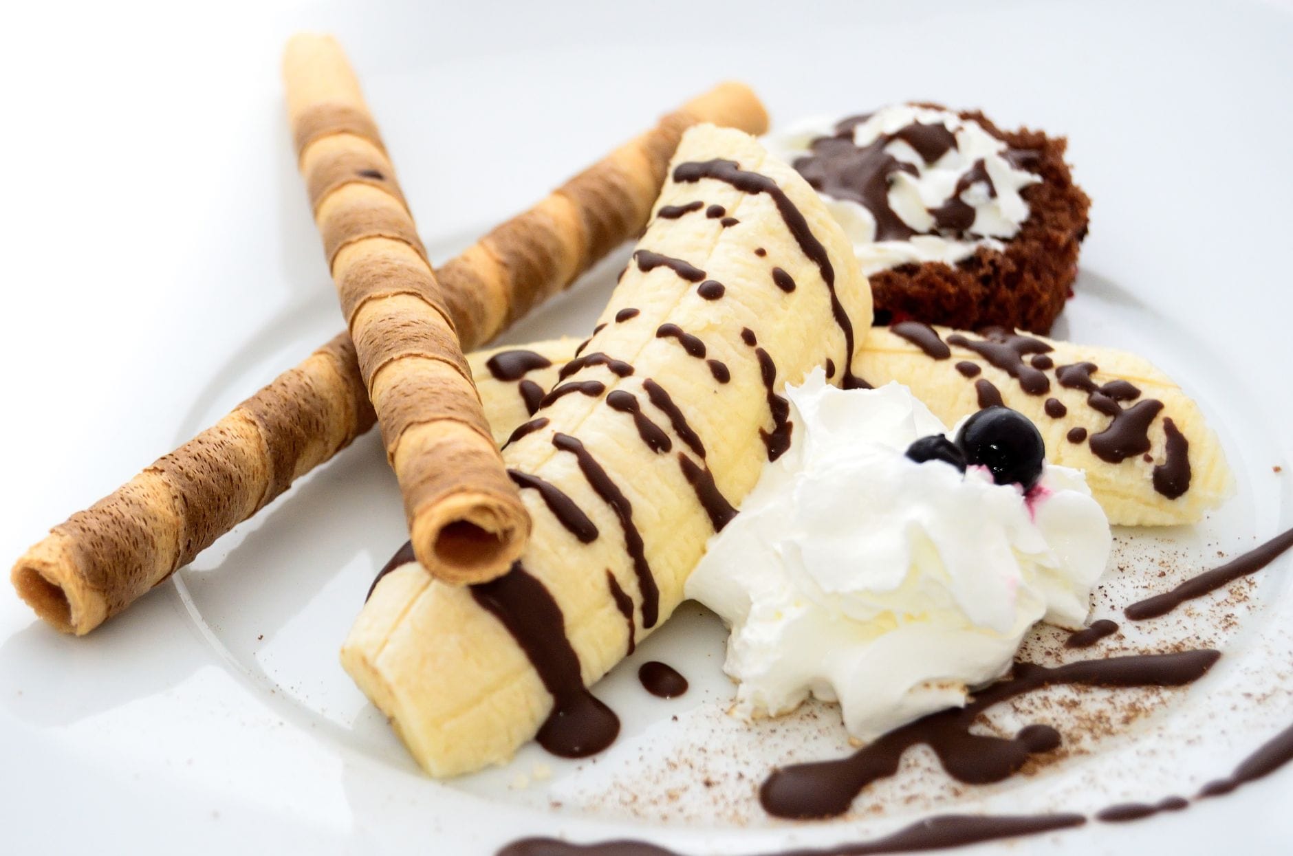 Deser bananowy z polewą czekoladową, bitą śmietaną i rurkami waflowymi