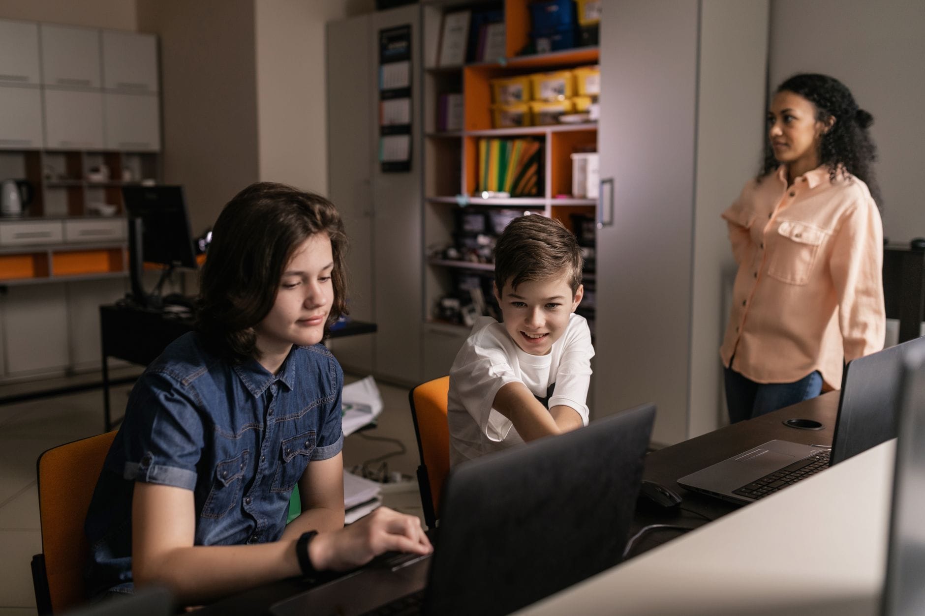 Nauczyciel nadzoruje uczniów pracujących na laptopach w klasie