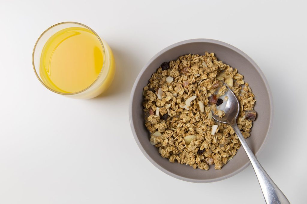 Granola w misce z łyżką i szklanką soku pomarańczowego